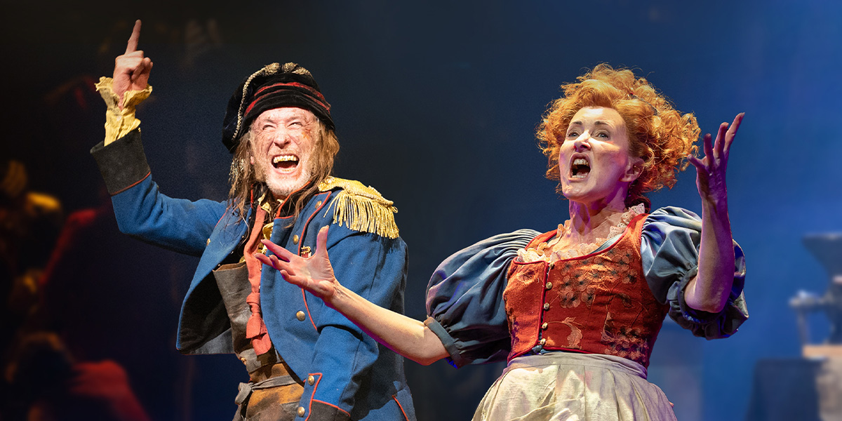 A man in a blue coat and a woman in a red dress passionately perform on stage.