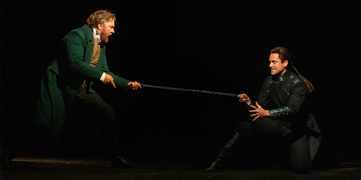 Killian Donnelly and Bradley Jaden in black costumes, standing on a stage with soft lighting.