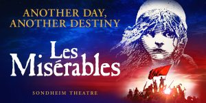 A ticket agent stands behind a counter, holding tickets for Les Misérables, with a red and gold backdrop.