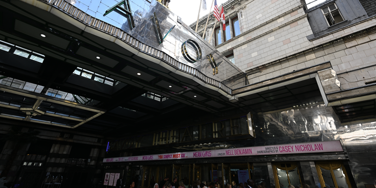 Exterior of Savoy Theatre, featuring a red marquee and ornate stonework against a clear blue sky.
