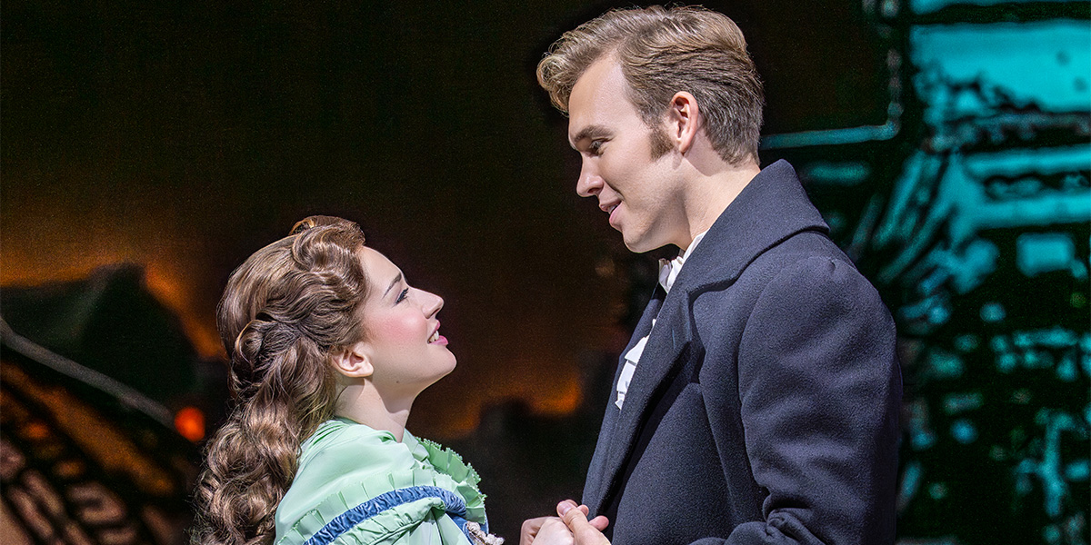 A woman in a green dress gazes lovingly at a man in a dark coat, both smiling.