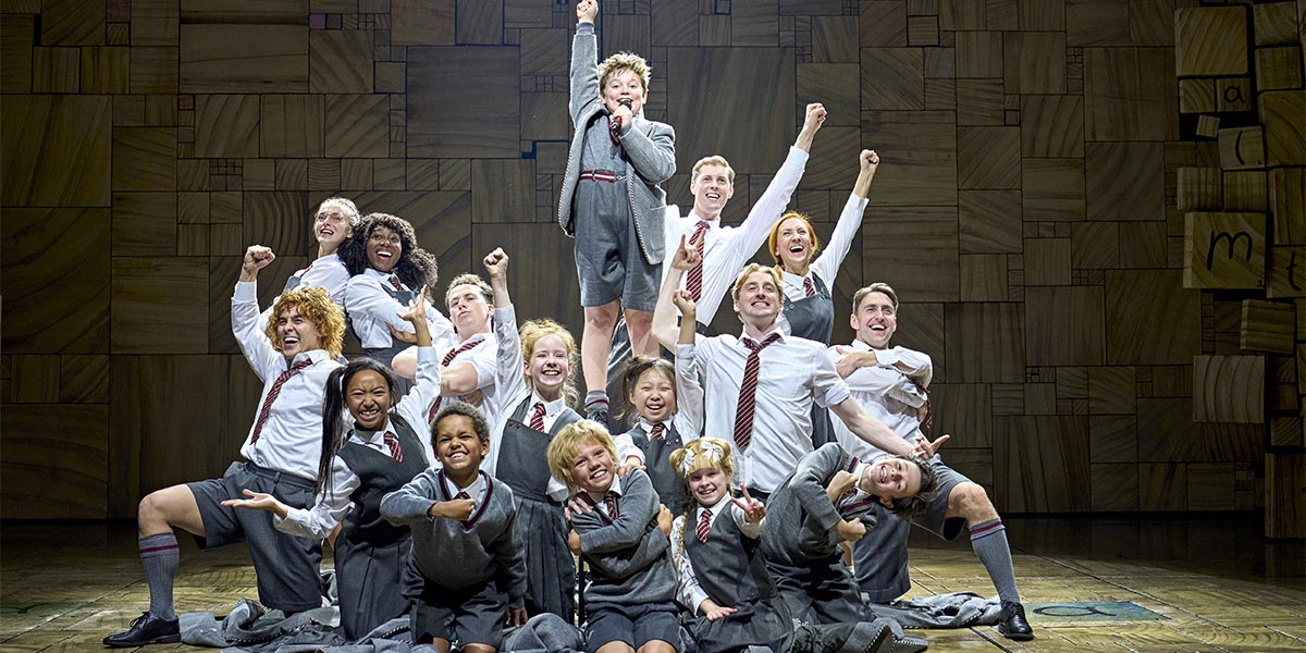 A scene from Matilda The Musical featuring actors in vibrant costumes performing on stage with dramatic lighting.