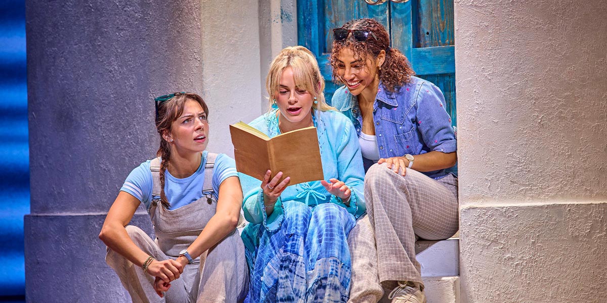 A scene from Mamma Mia! featuring actors in vibrant costumes, performing energetically on a colourful stage.