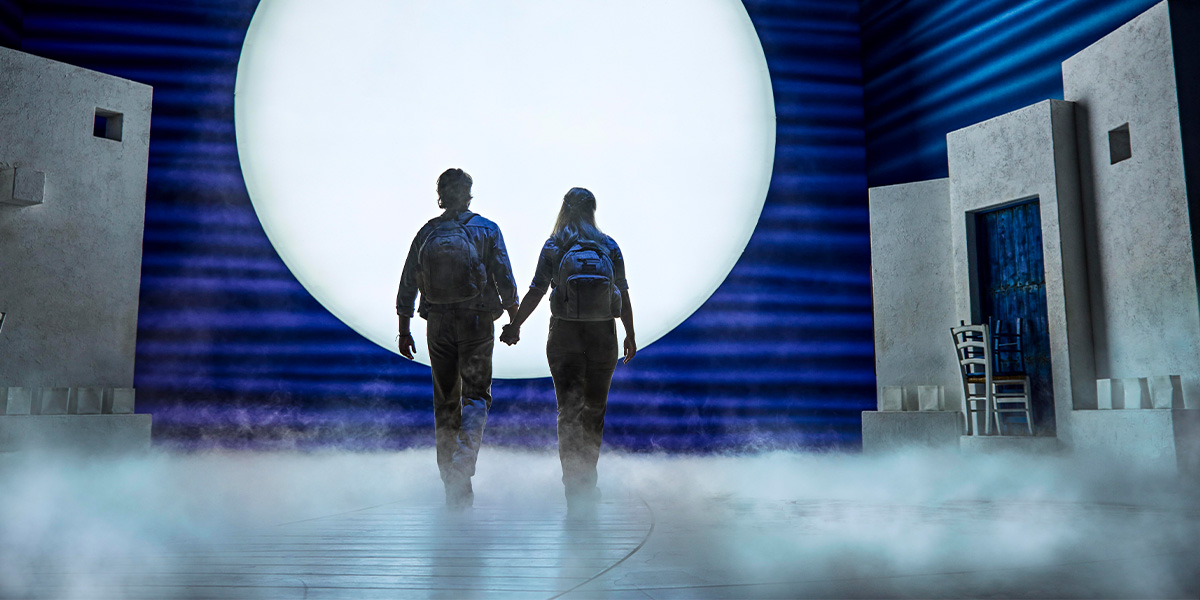 Two figures walk hand-in-hand towards a large illuminated circle, surrounded by fog and minimalist scenery.
