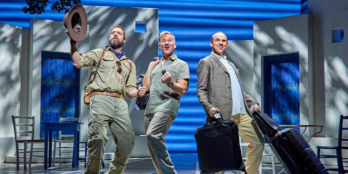 A scene from Mamma Mia! featuring performers in colourful costumes, dancing joyfully on stage.