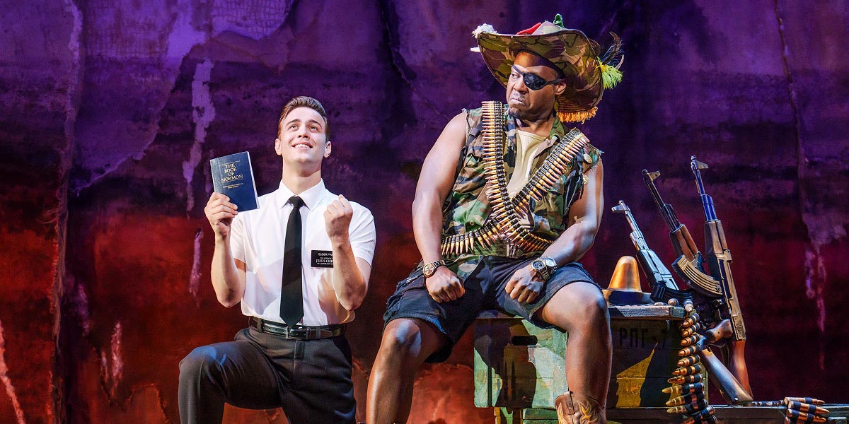 A scene from The Book of Mormon featuring characters in vibrant costumes, engaged in a dramatic moment.