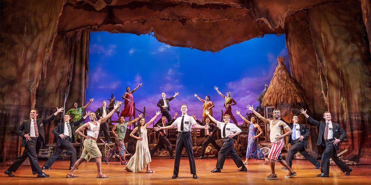 A vibrant stage scene with performers in varied costumes, striking poses against a colourful backdrop.