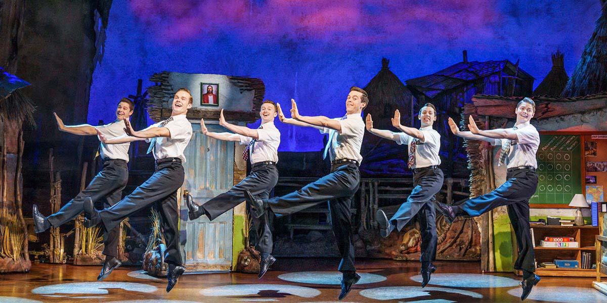 A scene from The Book of Mormon featuring characters in vibrant costumes, with a dramatic backdrop.