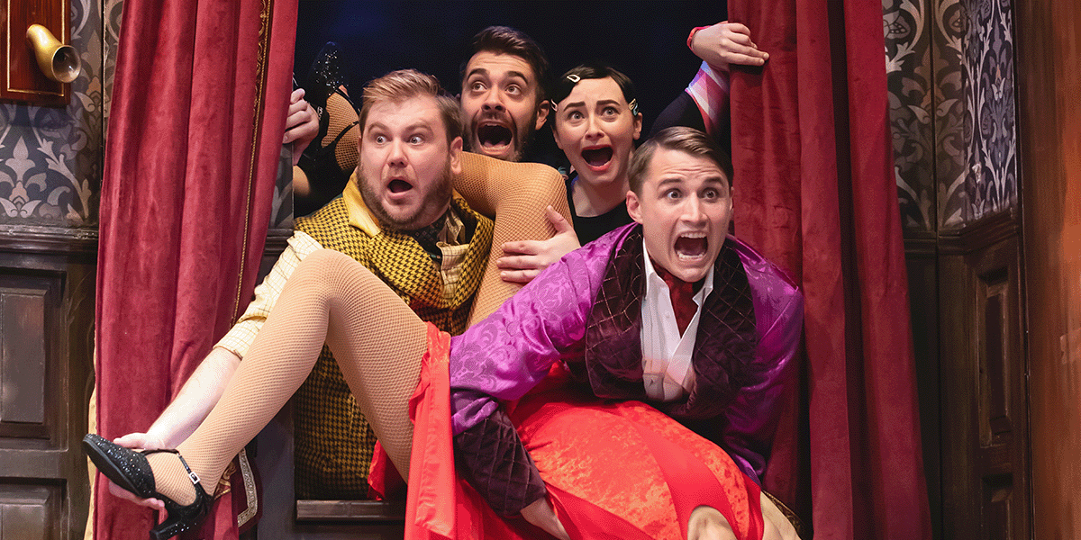 Four actors in vibrant costumes express surprise, emerging from behind red curtains in a theatrical setting.