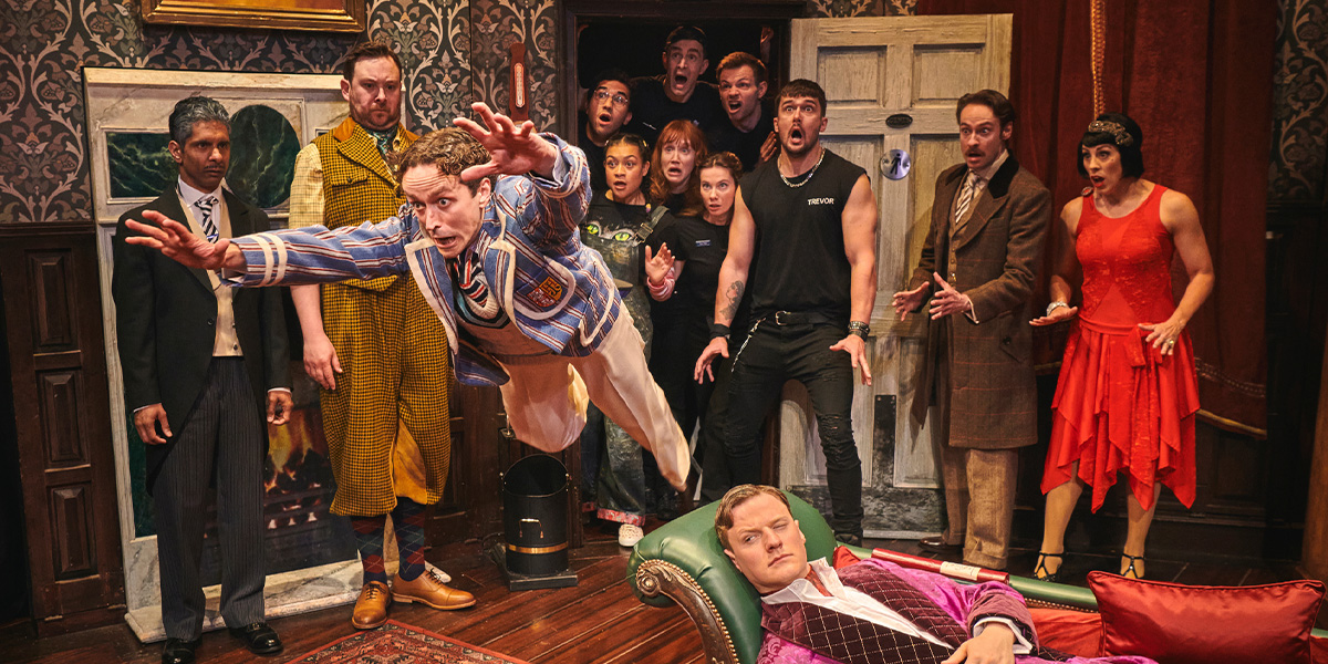A chaotic scene from "The Play That Goes Wrong," featuring actors in mismatched costumes amidst scattered props.