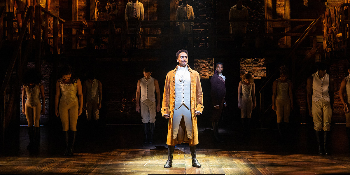 Alex Sawyer as Alexander Hamilton and Jay Perry as Aaron Burr perform on stage with the ensemble.