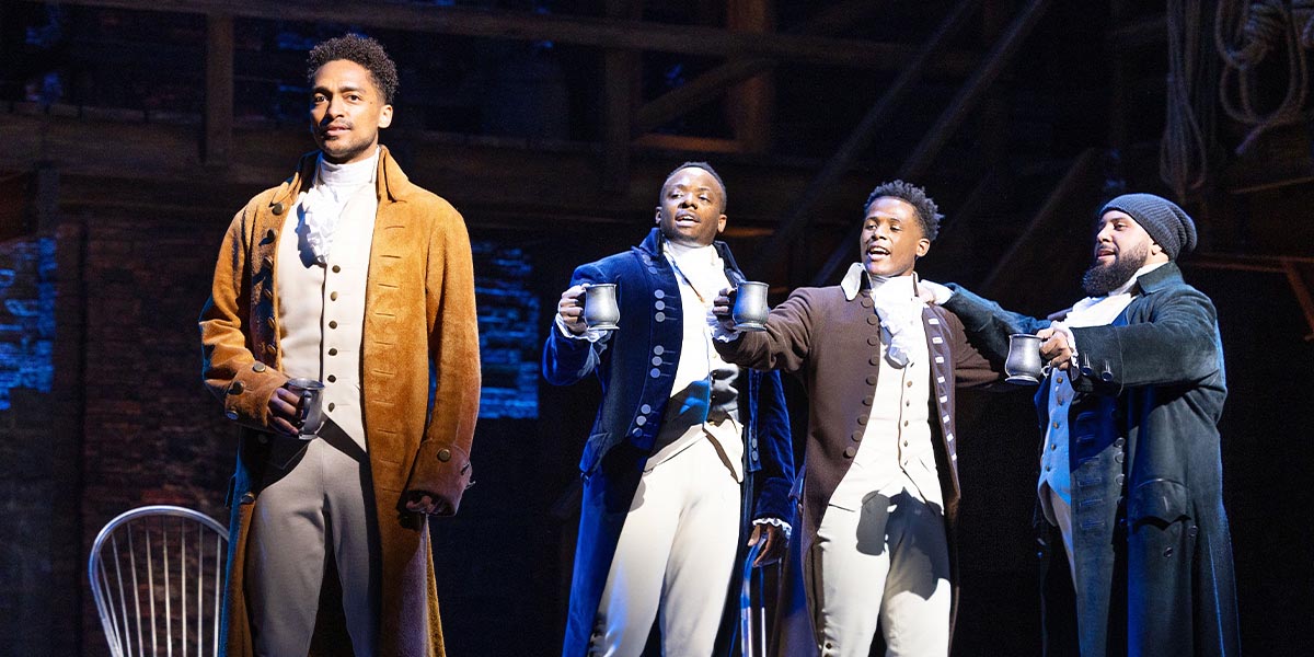 Alex Sawyer as Alexander Hamilton, Yeukayi Ushe as Marquis de Lafayette, Jordan Benjamin as John Laurens, and Jordan Castle as Hercules Mulligan, performing together on stage.