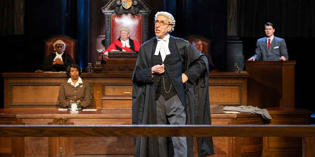 A courtroom scene with a barrister speaking, a judge seated, and witnesses observing.