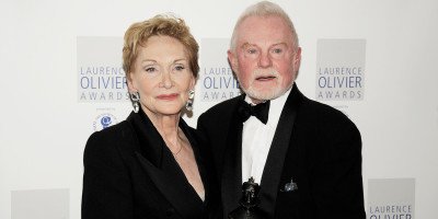 A woman in a black outfit and a man in a tuxedo pose together at an awards event.