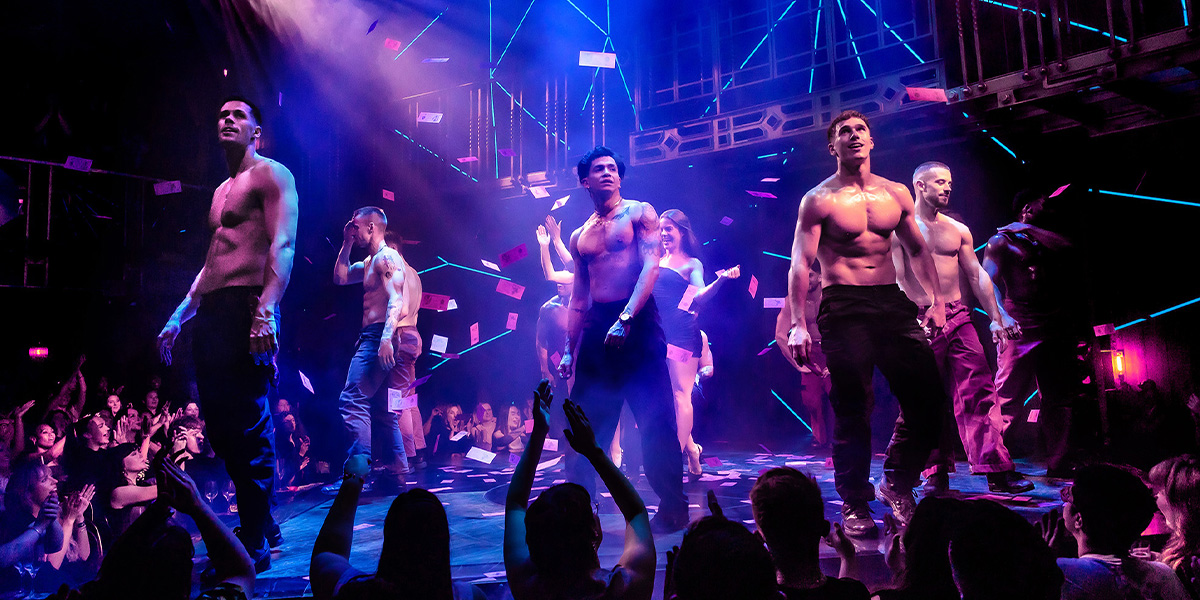 A performer in a sequined costume strikes a dynamic pose on stage, illuminated by vibrant stage lights.