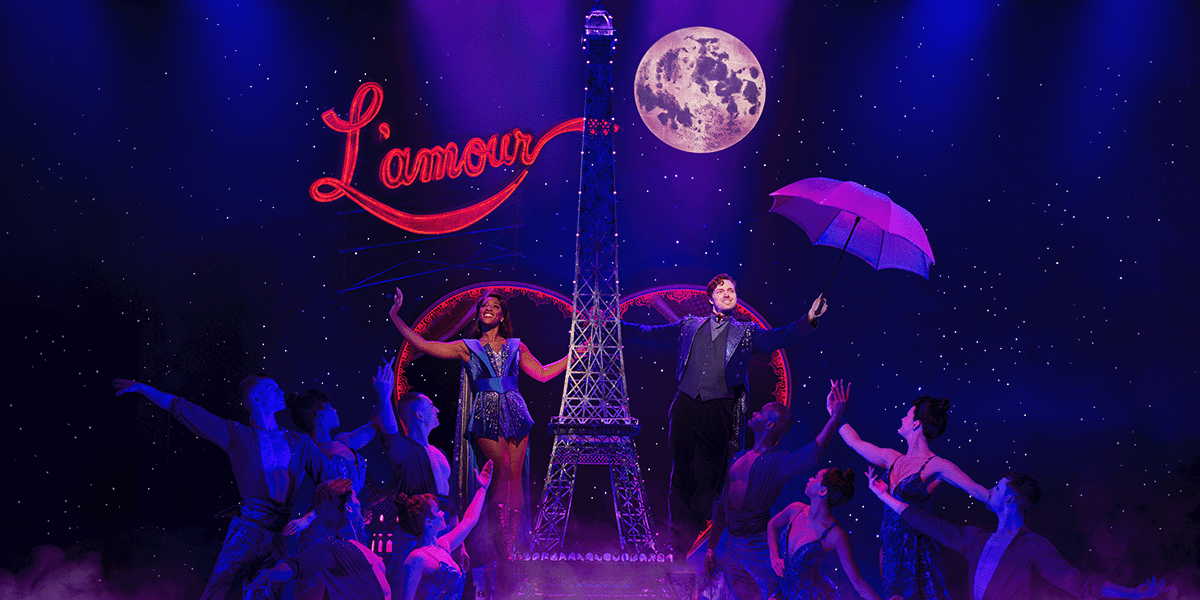 A performer in a red and black costume poses dramatically on stage, with vibrant stage lights in the background.