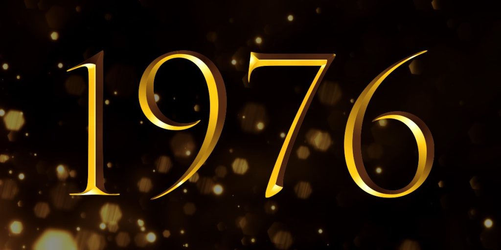 A group of elegantly dressed individuals stands on stage, holding awards, with a spotlight illuminating them.