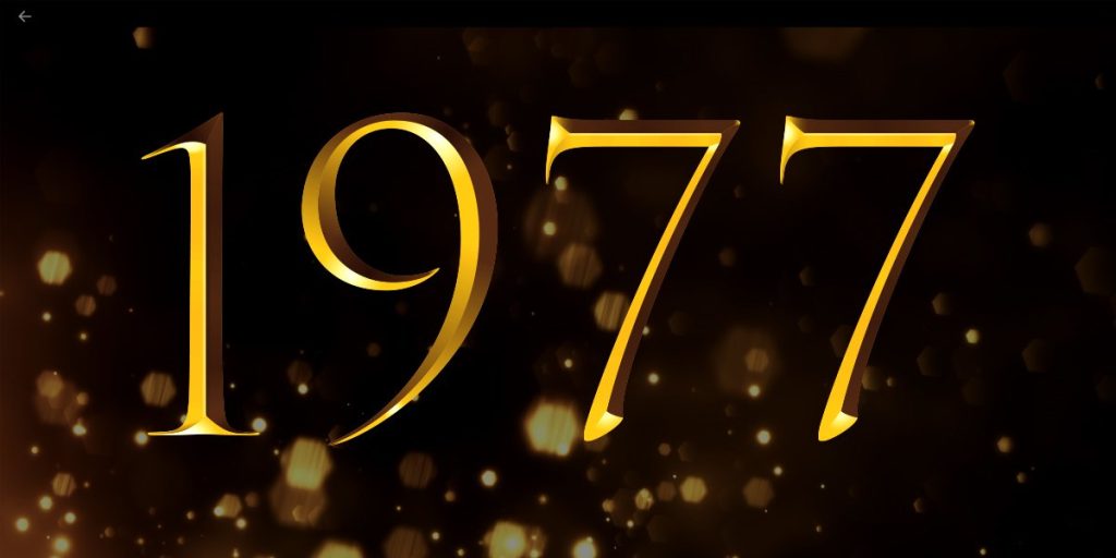 A group of elegantly dressed individuals stands on stage, holding awards, with a spotlight illuminating them.