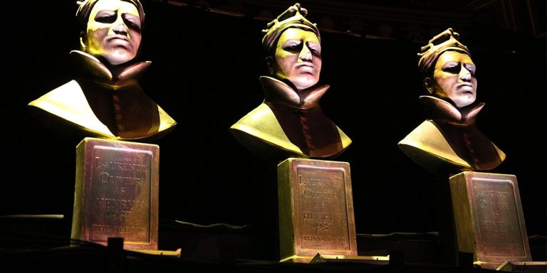 Three bronze busts with plaques, illuminated against a dark background, depicting solemn figures wearing crowns.
