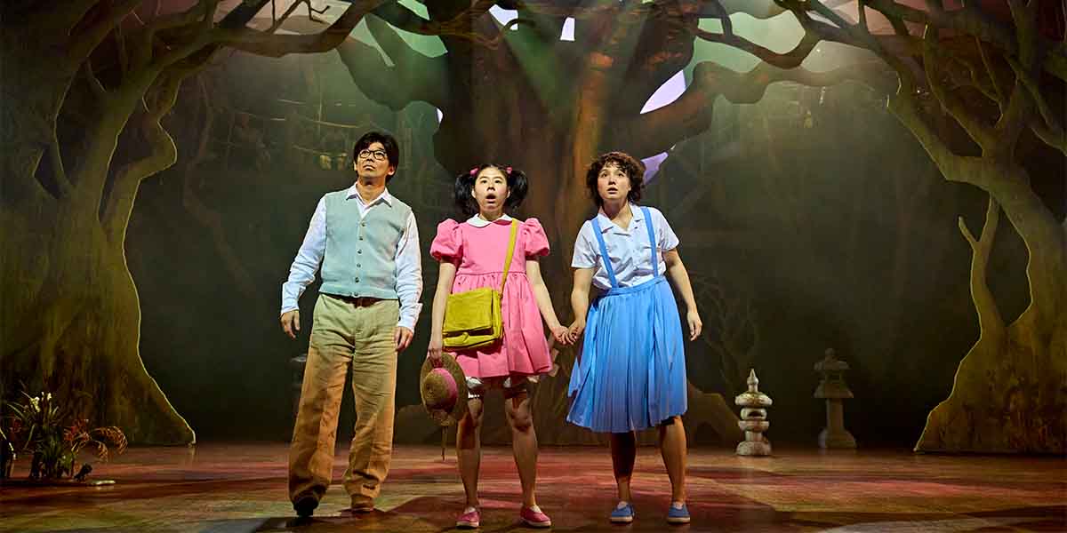 Three characters stand together, looking surprised, in front of a large, stylised tree backdrop.