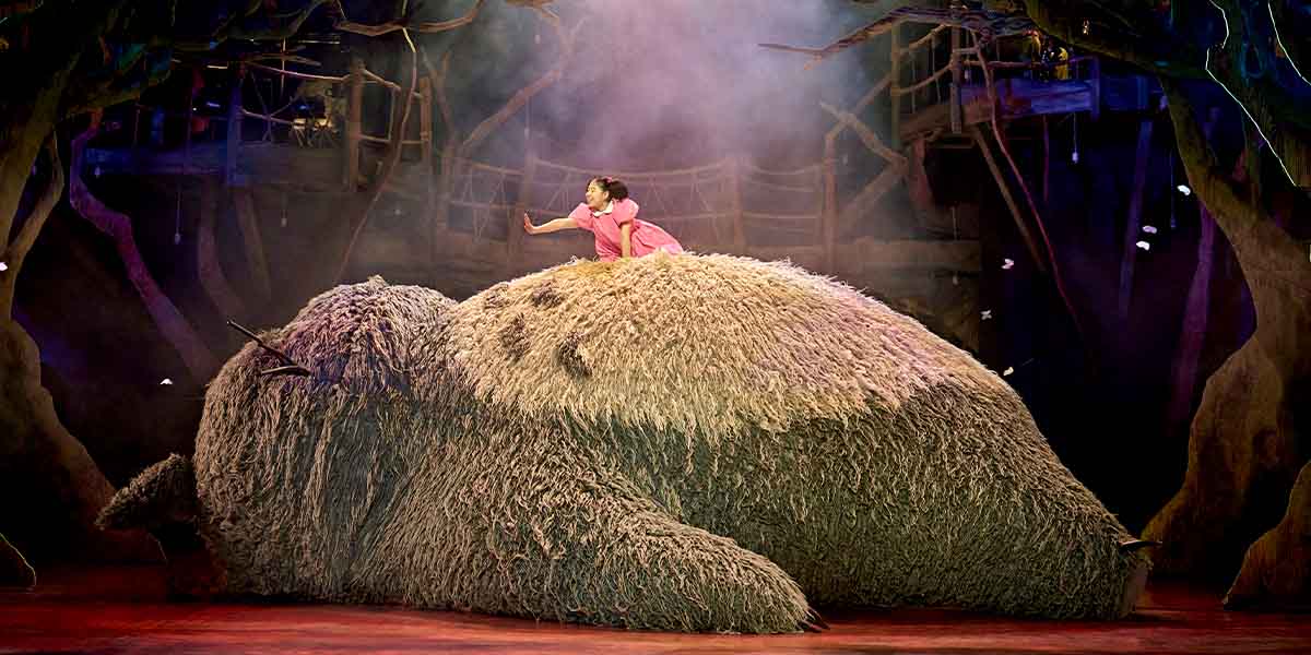 A scene from RSC's My Neighbour Totoro, featuring characters in vibrant costumes amidst a whimsical forest backdrop.