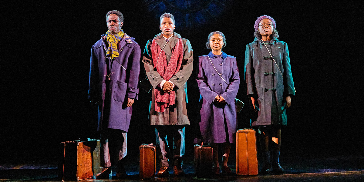 Four people stand on stage with luggage at their feet.