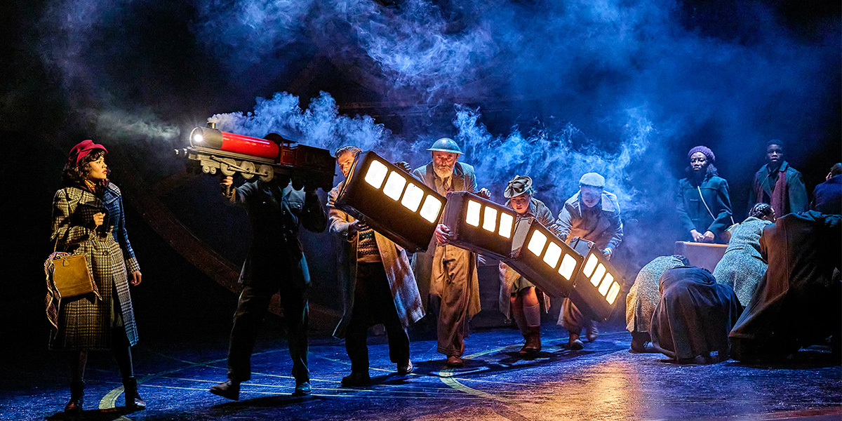 A black and red steam train is moving across the stage.