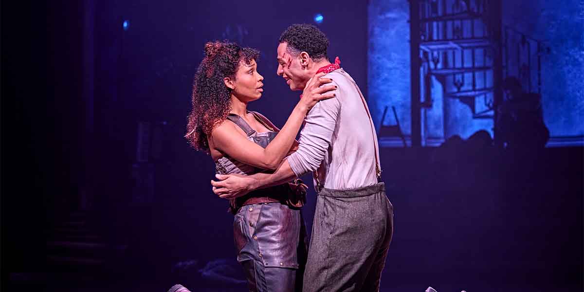 Bethany Antonia and Marley Fenton embrace on stage, illuminated by dramatic lighting and a dark background.