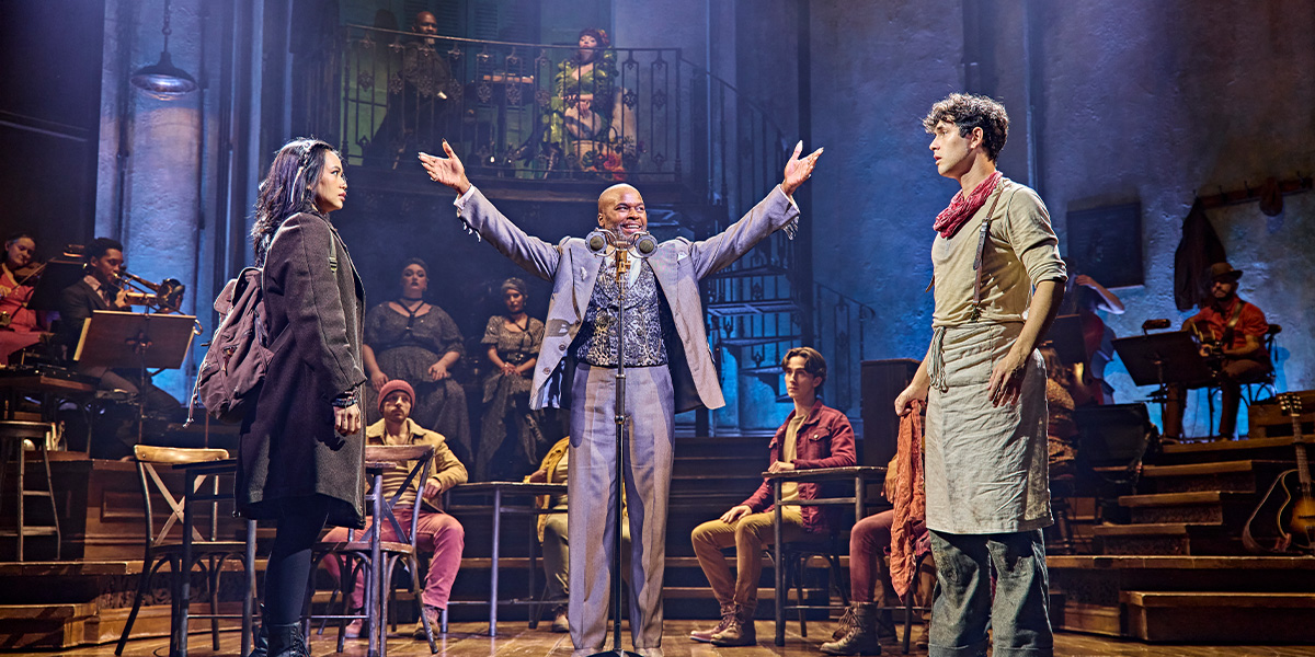 Desmonda and Cedric Neal perform on stage, wearing vibrant costumes, with dramatic lighting and a dark backdrop.