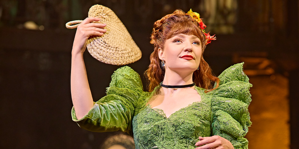 Nicola Roberts performs on stage in a flowing, dark dress, surrounded by dramatic lighting and set design.