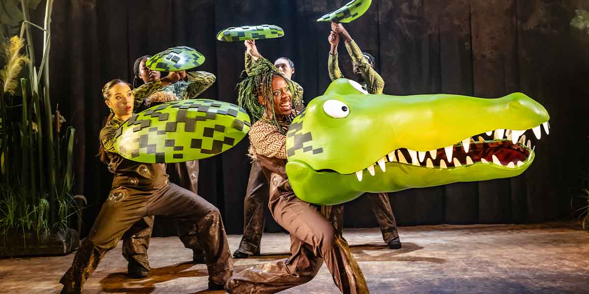 Chelsea Da Silva performs as The Enormous Crocodile, surrounded by cast members holding green props.