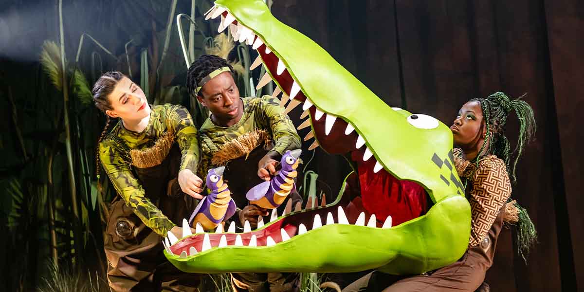 Ciara Hudson, Jordan Eskeisa, and Chelsea Da Silva perform with a large green crocodile puppet on stage.