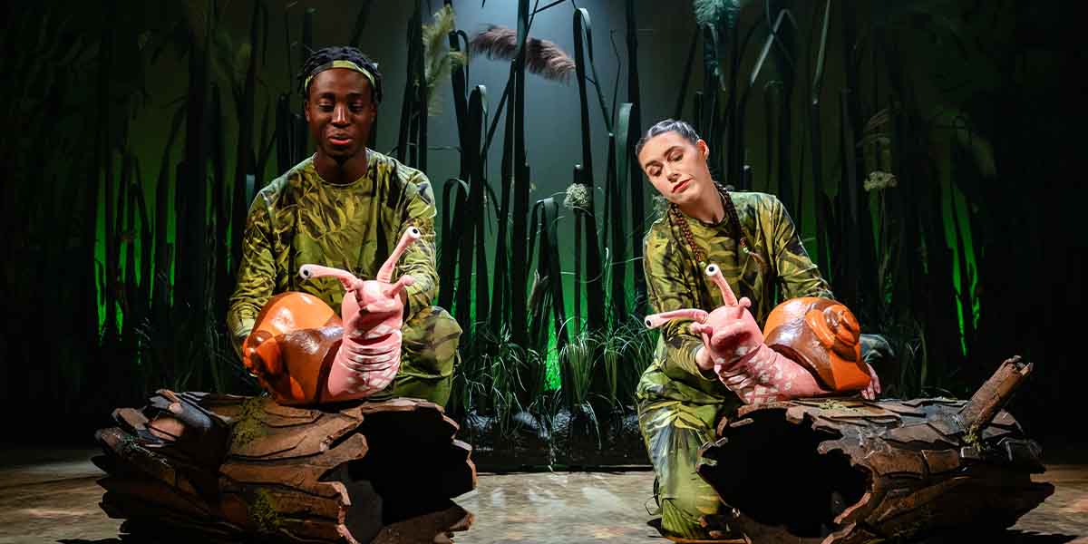 Jordan Eskeisa and Ciara Hudson, dressed in green, pose with snail props on a wooden log.