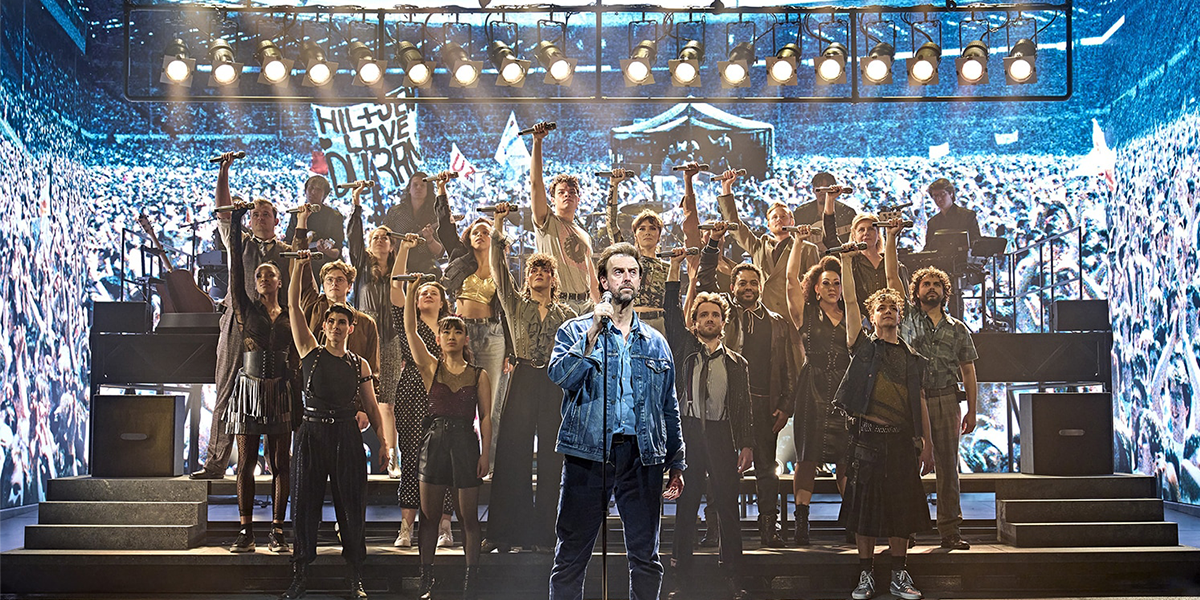 A vibrant stage with performers in colourful costumes, singing passionately under bright lights during a live musical event.