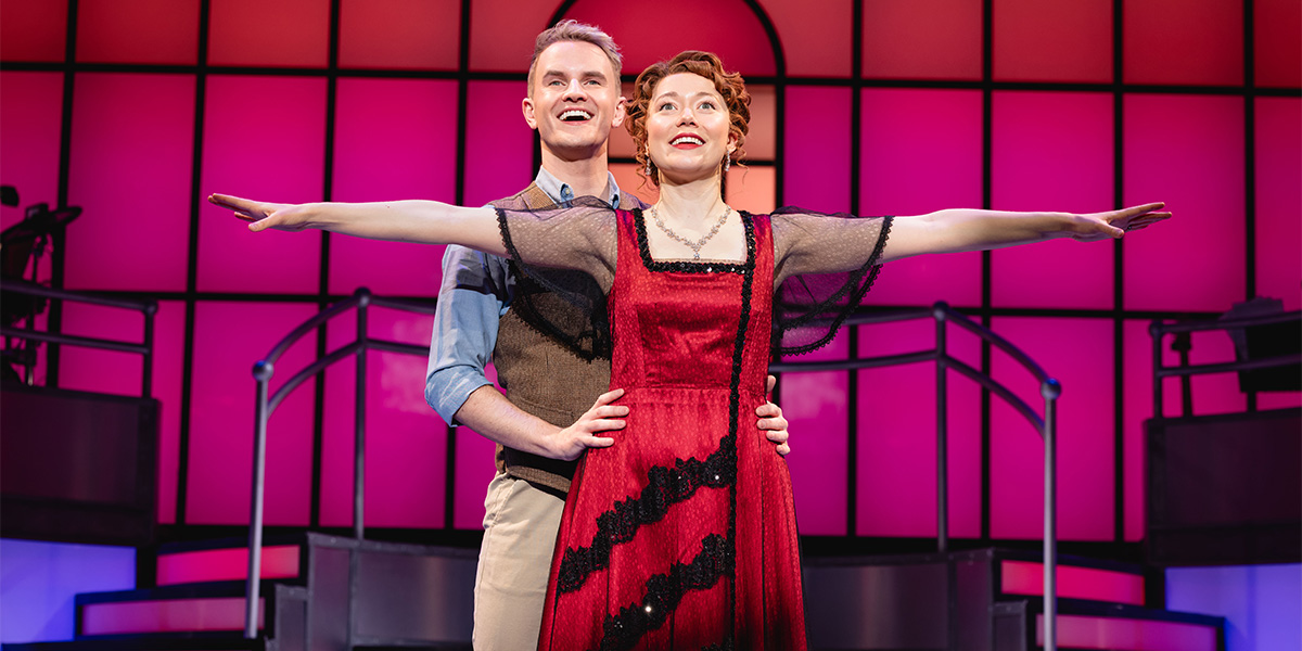 A senior person stands confidently, smiling, wearing a dark suit against a blurred background of soft colours.