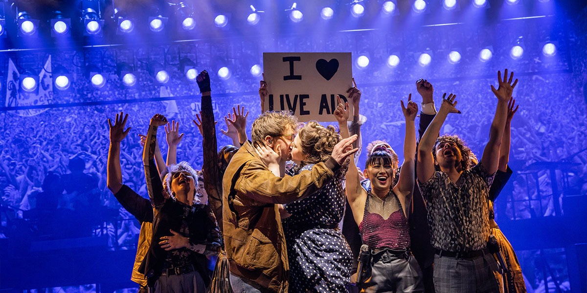 A performer in a vibrant costume sings passionately on stage, with colourful lights illuminating the background.