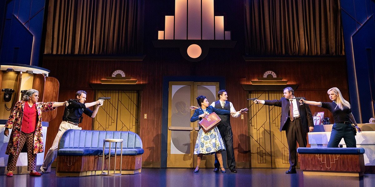 Two people stand in the centre surrounded by people who are aiming guns at them.