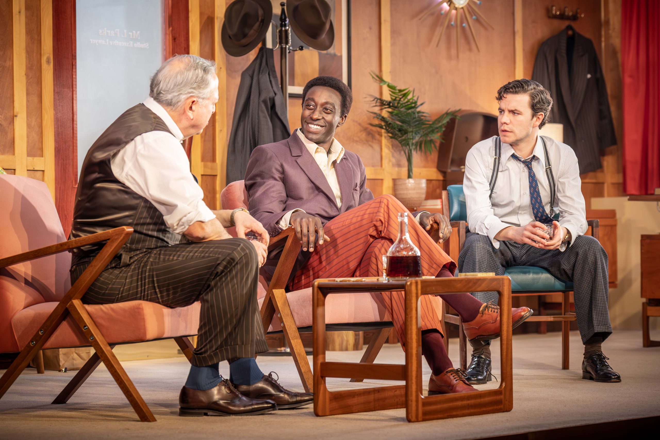 Three people are sitting around a small brown table. They are laughing.
