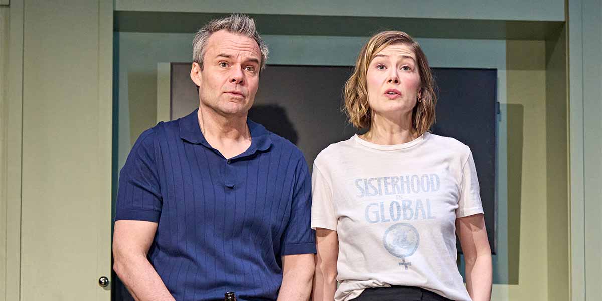 Jamie Glover and Rosamund Pike perform in "Inter Alia," with Glover in a blue shirt and Pike in a graphic tee.