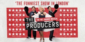 A group of four actors in theatrical costumes, performing on stage with dramatic lighting and a red curtain backdrop.