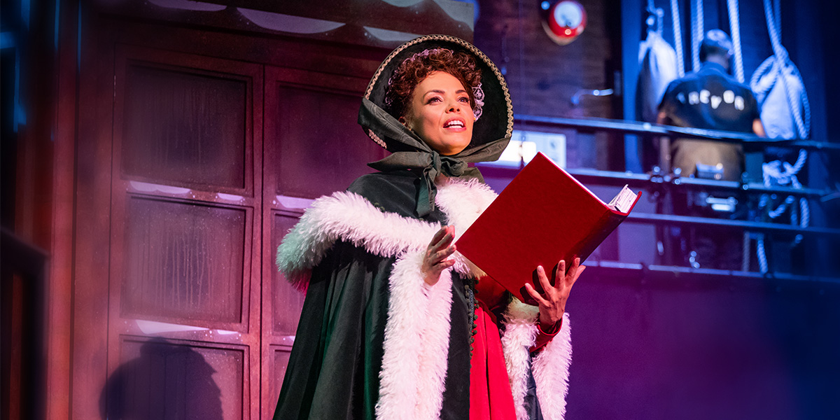 Sasha Frost as a character in Christmas Carol Goes Wrong, wearing a festive costume with red and green accents.