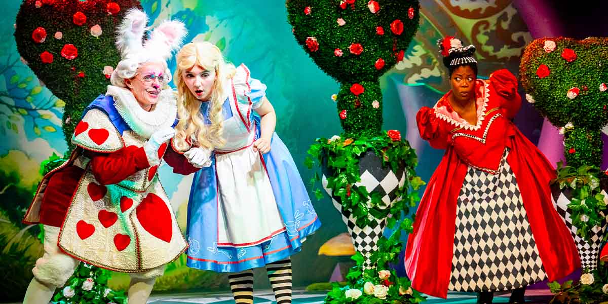 Clare Brice as the White Rabbit, Charlotte Bradley as Alice, and Honey Gabriel in ensemble costumes.
