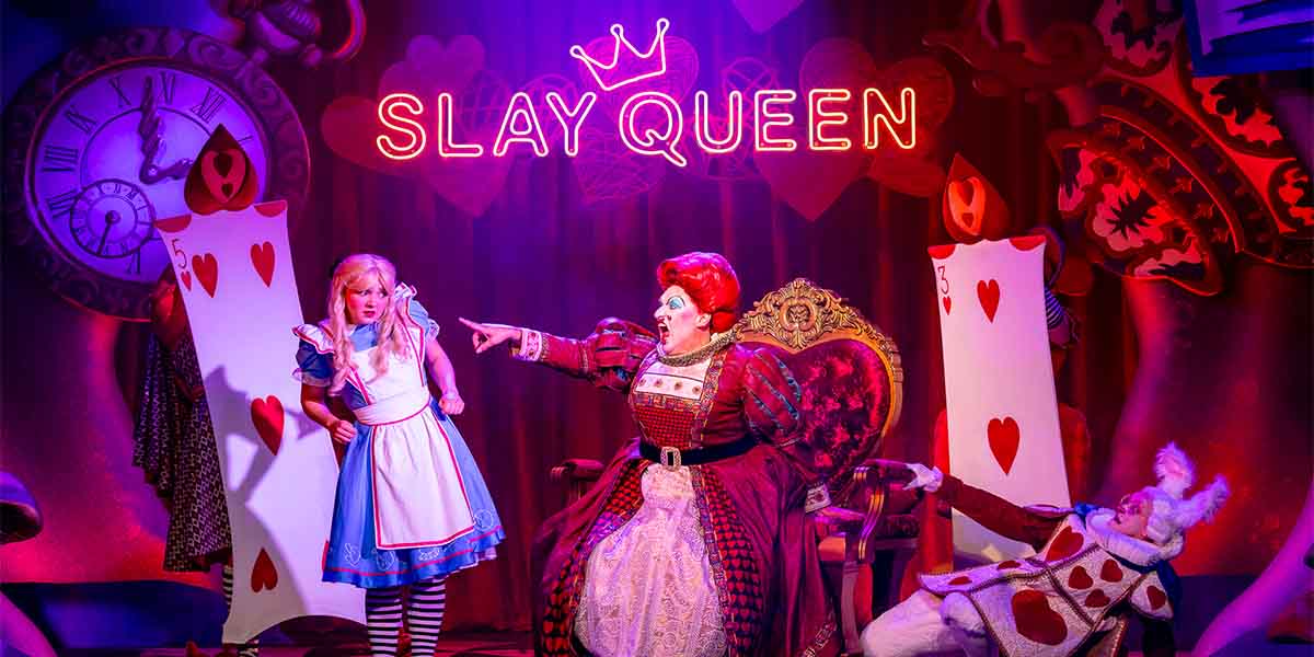 Charlotte Bradley as Alice stands beside Daniel Page as the Queen of Hearts, gesturing dramatically.