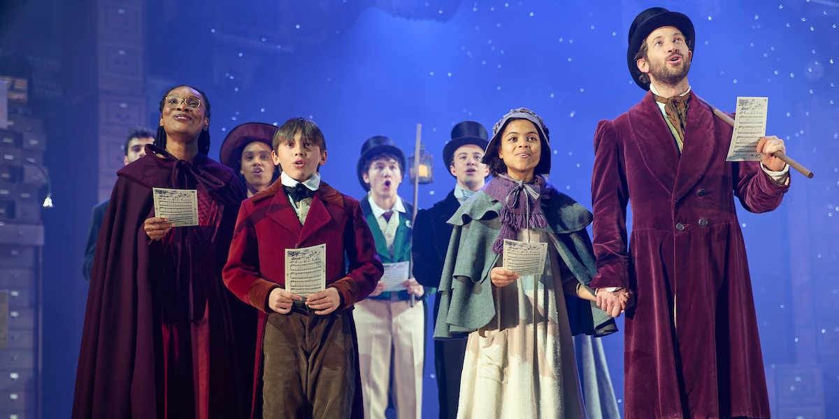 A scene from A Christmas Carol with actors in Victorian costumes, featuring rich colours and dramatic lighting.