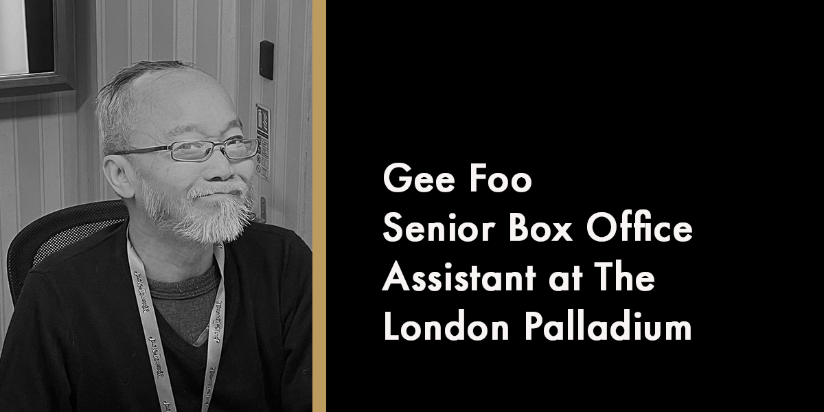 Gee Foo smiling, with grey hair and beard, seated against a wooden background.