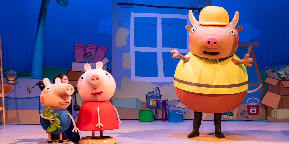 George and Peppa Pig stand beside Mr Bull, smiling, with a colourful stage backdrop featuring Peppa Pig characters.