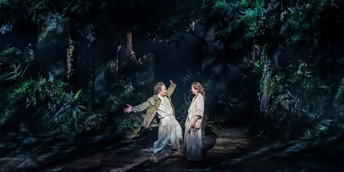 Two people stan together in the woods.