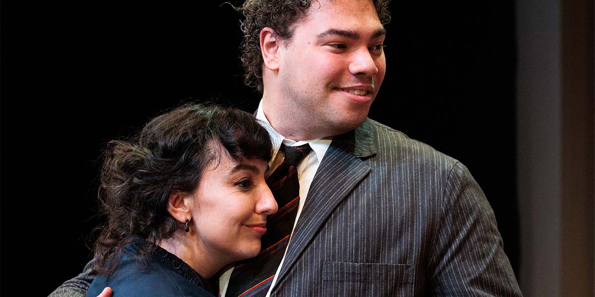 Ailsa Joy and Daniel Abbot stand together, smiling, in a warmly lit setting with wooden decor.