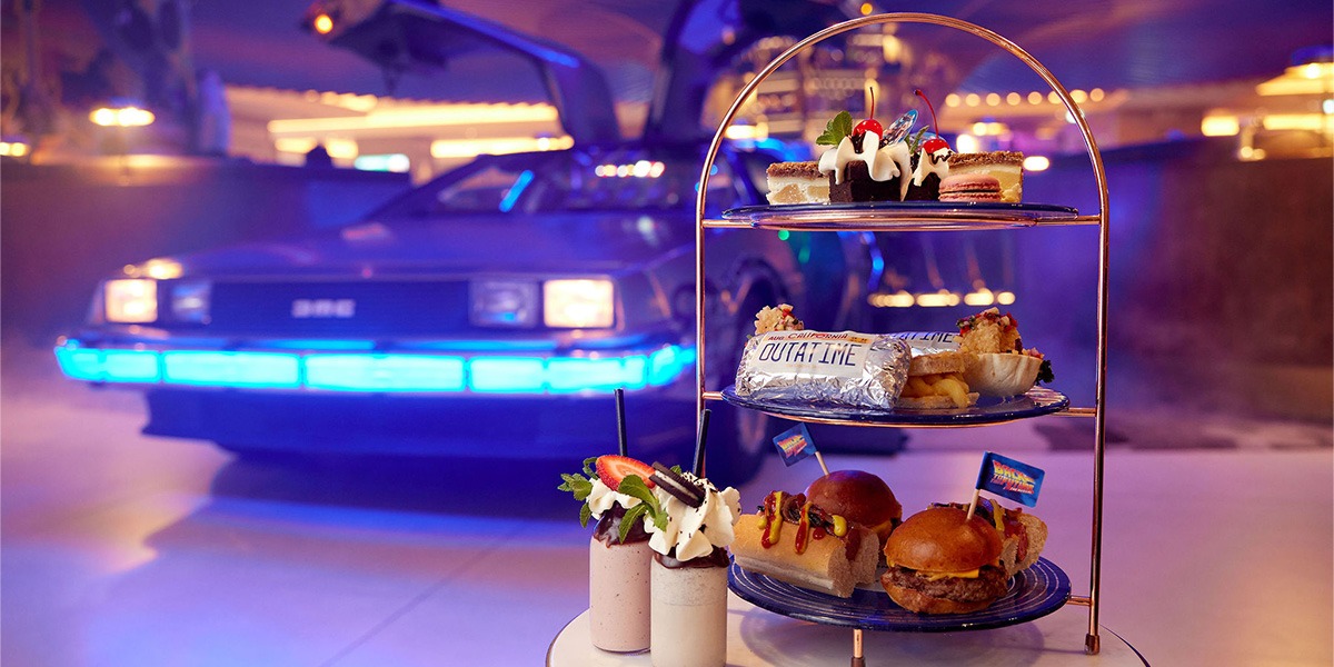 An assortment of American diner miniature snacks on an afternoon tea rack, in front of a Delorean car