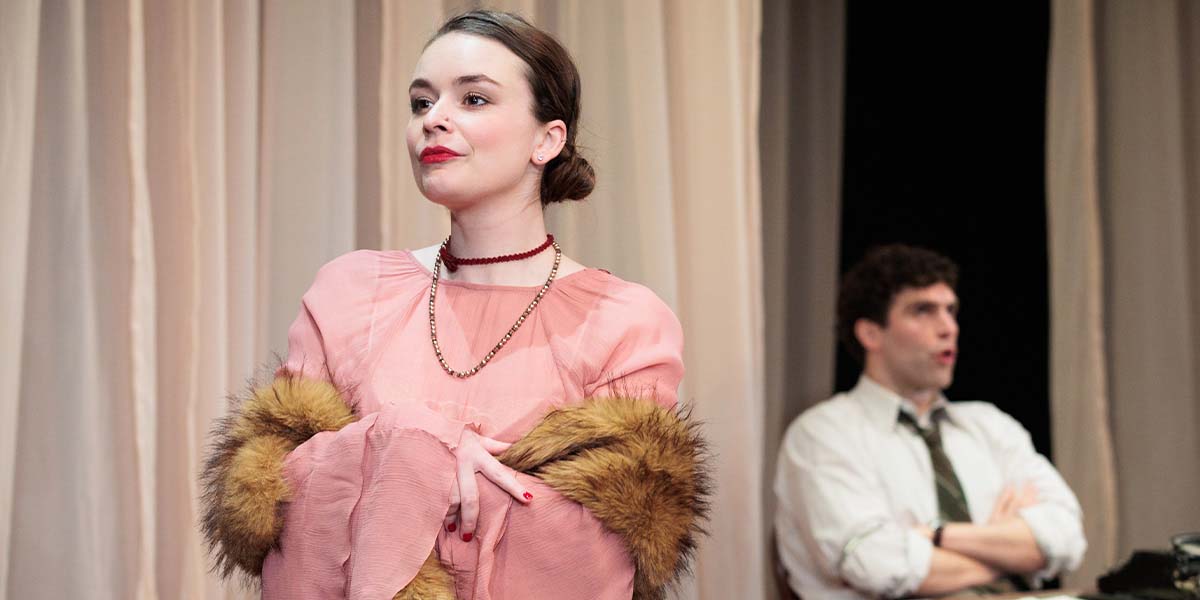 Zoe Goriely wears a pink dress with fur sleeves, while Ewan Miller sits in the background.